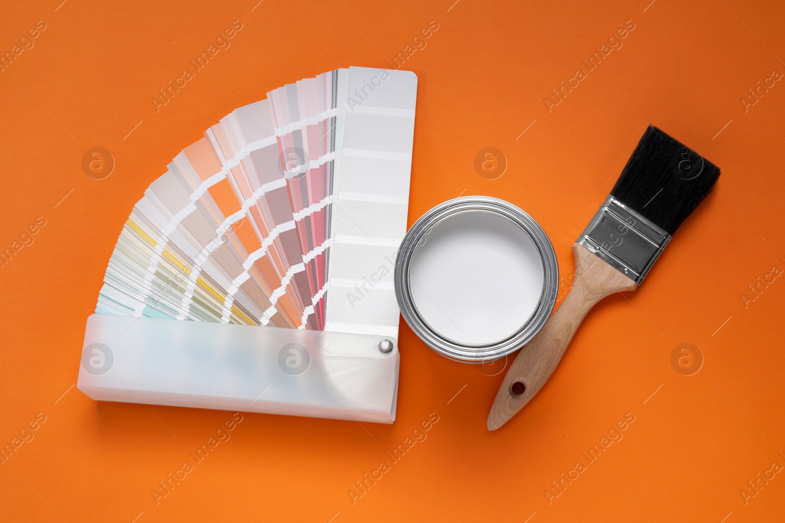 Photo of Can with white paint, brush and color palette on orange background, flat lay