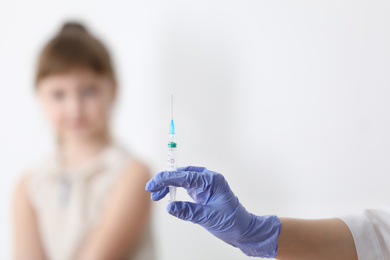 Doctor holding syringe with chickenpox vaccine and child on background, closeup. Varicella virus prevention