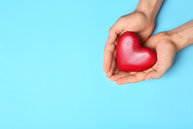 Photo of Young man holding red heart on light blue background, top view with space for text. Donation concept