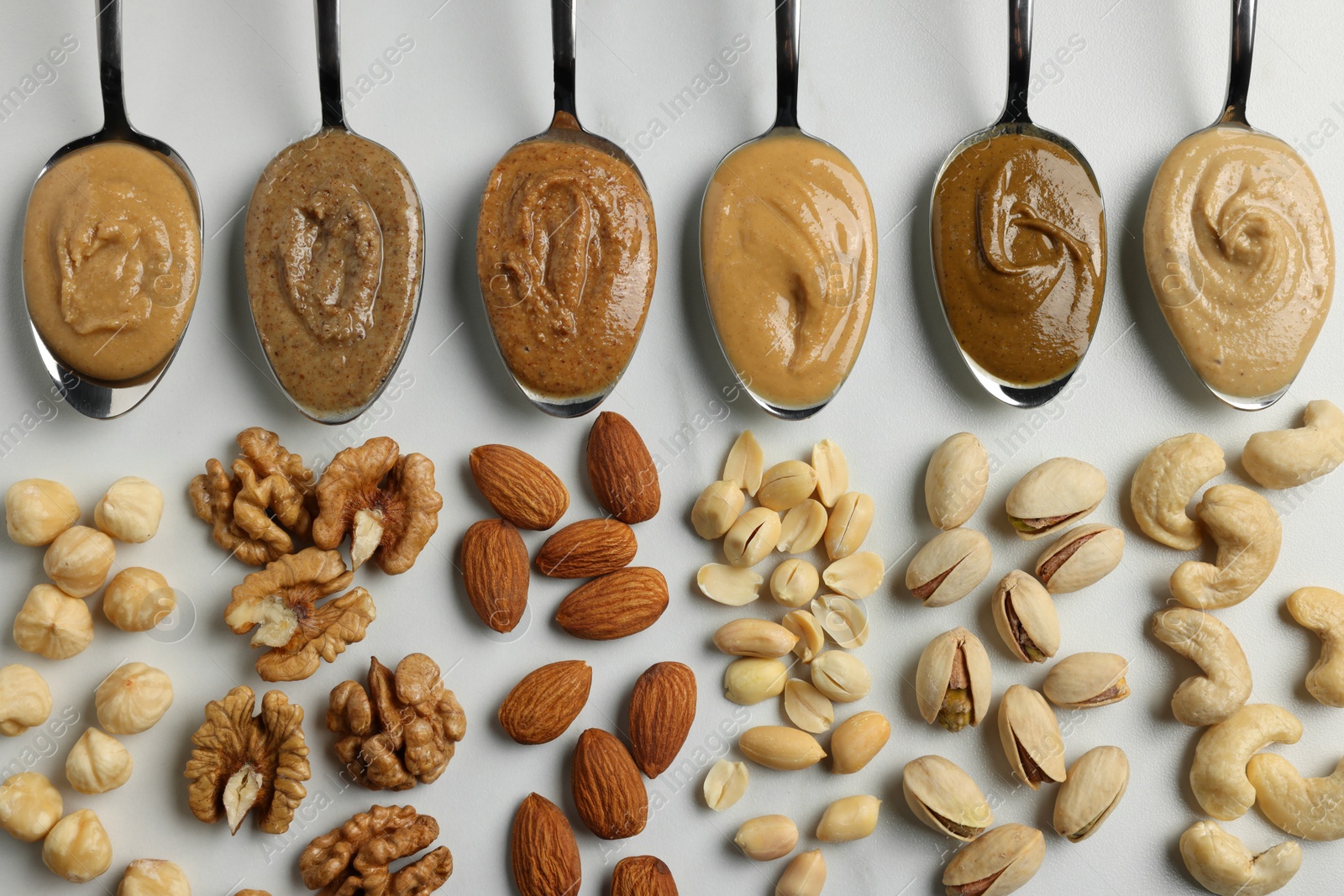 Photo of Tasty nut butters in spoons and raw nuts on white table, flat lay