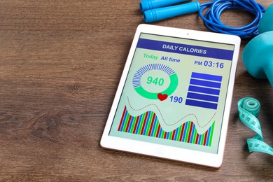 Tablet with weight loss calculator application, skipping rope and measuring tape on wooden table. Space for text