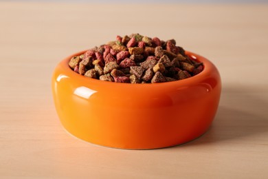 Photo of Dry food in orange pet bowl on wooden surface, closeup