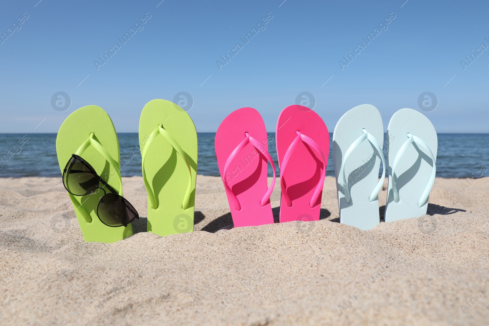 Photo of Stylish colorful flip flops and sunglasses on beach sand