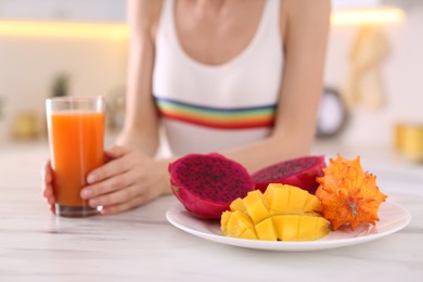 Woman with fresh juice and exotic fruits at table in kitchen, closeup
