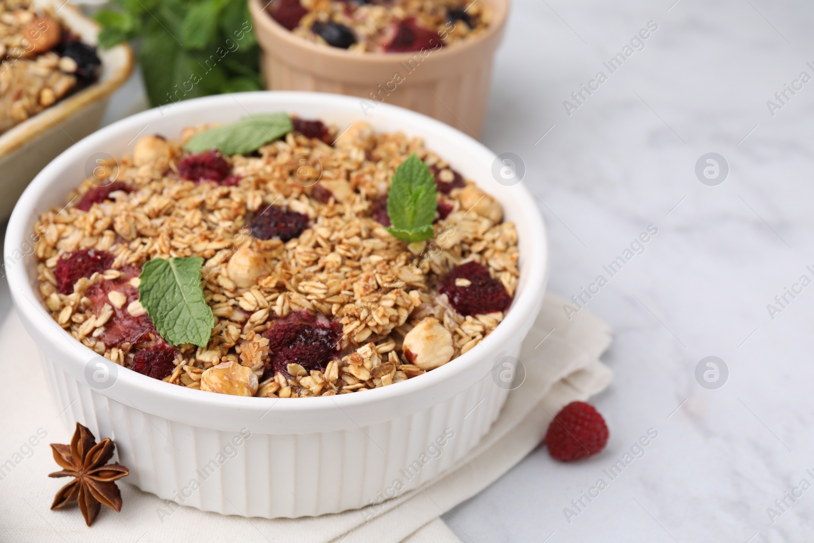 Photo of Tasty baked oatmeal with berries, nuts and anise star on white marble table, closeup. Space for text