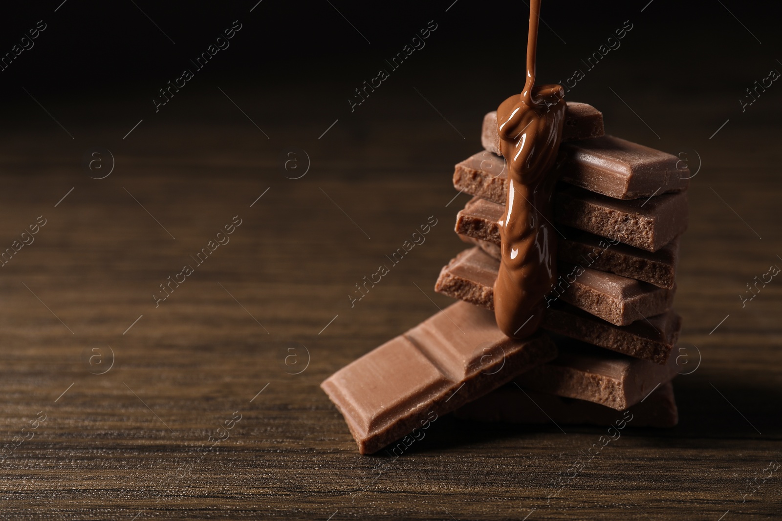 Photo of Pouring tasty milk chocolate paste onto pieces on wooden table, closeup. Space for text