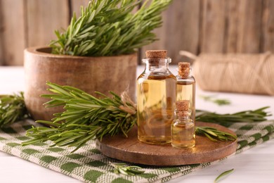 Essential oil in bottles and rosemary on white wooden table