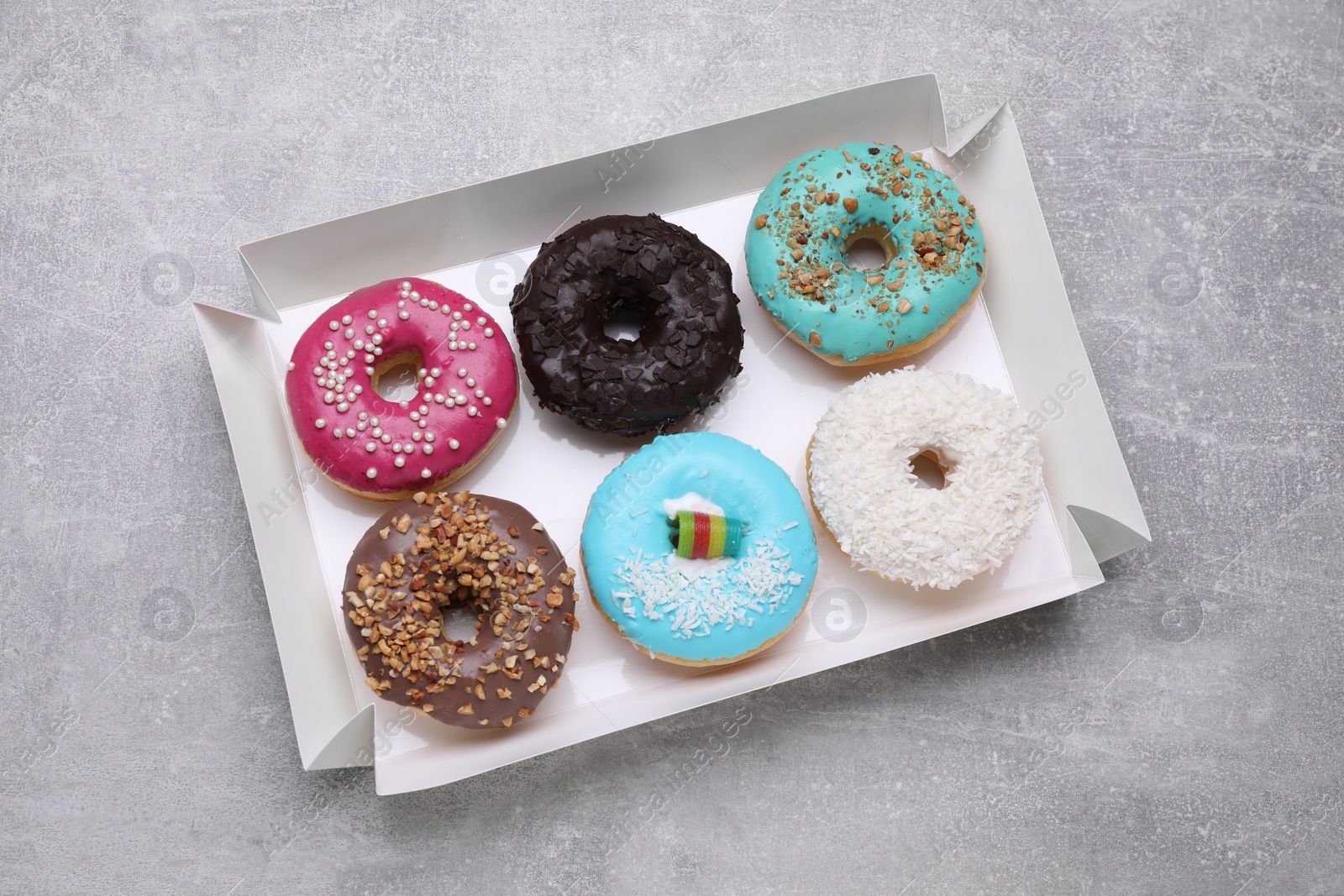 Photo of Box with different tasty glazed donuts on light grey table, top view