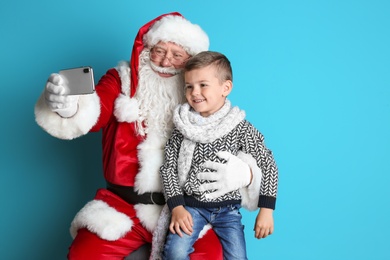 Photo of Authentic Santa Claus taking selfie with little boy on color background