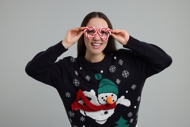 Photo of Happy young woman in Christmas sweater and funny glasses on grey background