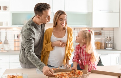 Photo of Pregnant woman and her family eating pizza in kitchen