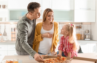 Pregnant woman and her family eating pizza in kitchen