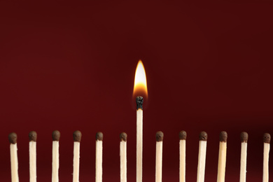 Photo of Burning match among unlit ones on red background, closeup