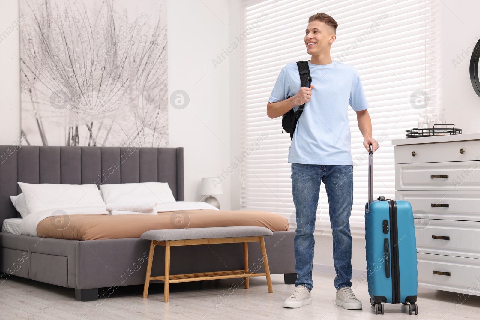 Photo of Smiling guest with suitcase and backpack exploring stylish hotel room