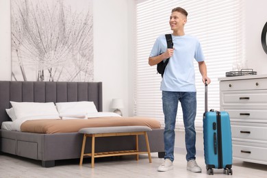 Smiling guest with suitcase and backpack exploring stylish hotel room