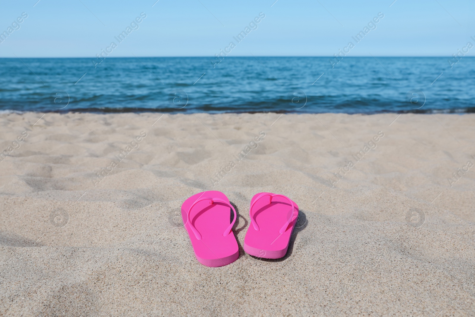 Photo of Stylish pink flip flops on beach sand, space for text