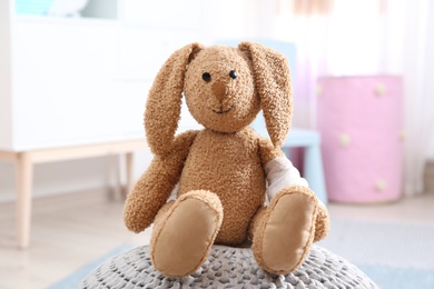 Photo of Toy bunny with bandaged pad on pouf indoors. Children's doctor