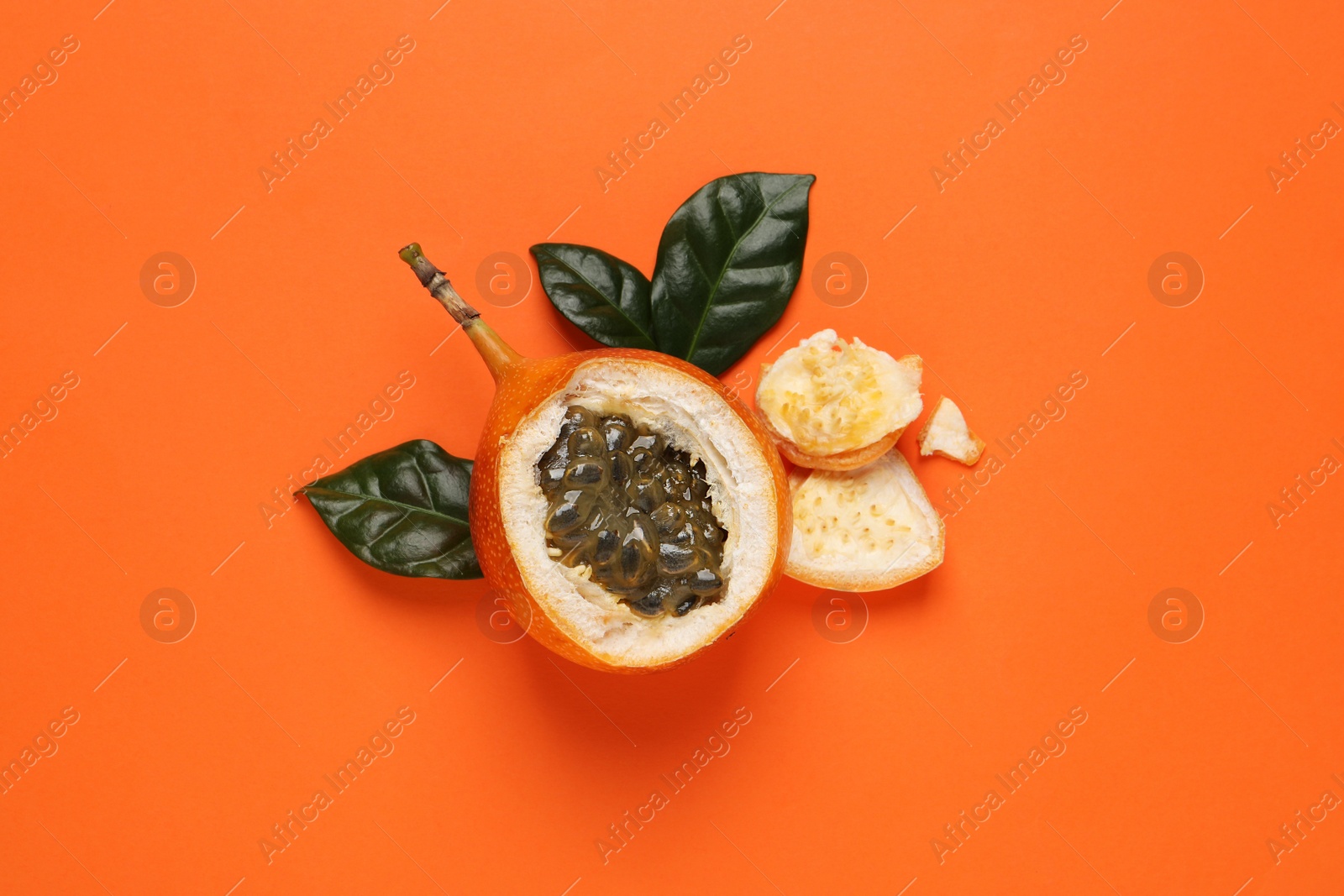 Photo of Delicious ripe granadilla with leaves on orange background, flat lay