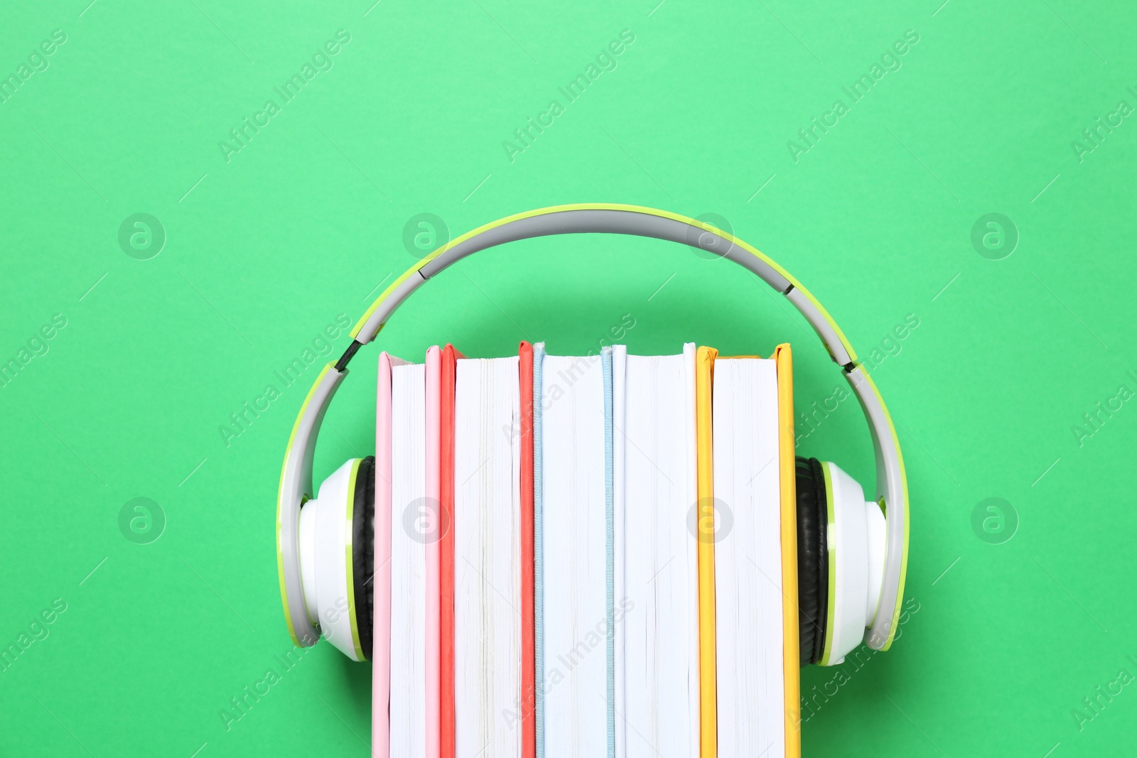 Photo of Books with modern headphones on green background, top view