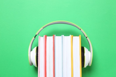 Books with modern headphones on green background, top view