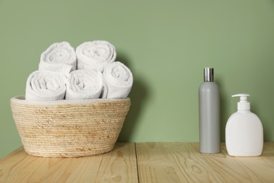 Wicker basket with clean towels and cosmetic products on wooden countertop near green wall