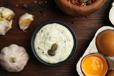 Photo of Creamy caper sauce in bowl and ingredients on wooden table, flat lay.