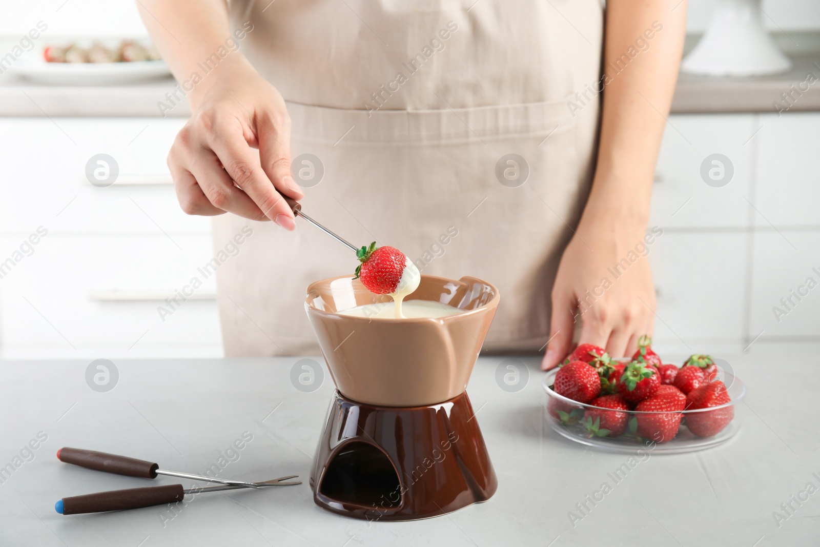 Photo of Woman dipping ripe strawberry into bowl with white chocolate fondue on table