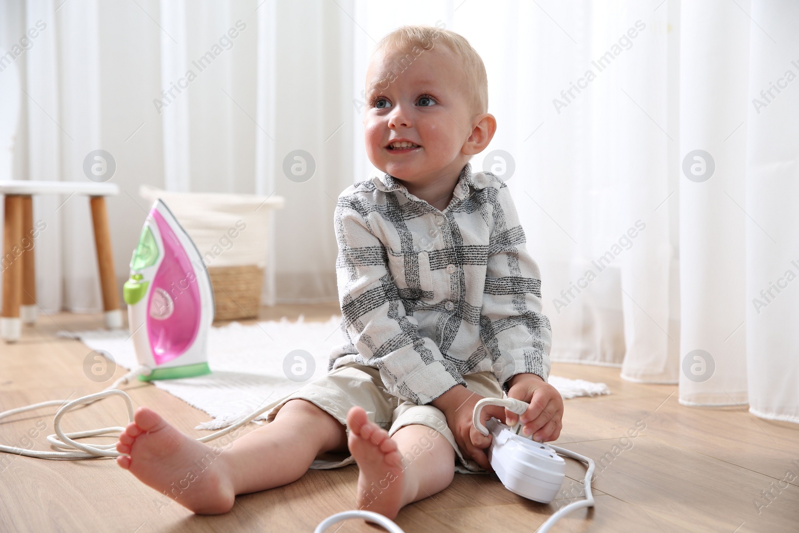 Photo of Little child playing with power strip and iron plug on floor at home. Dangerous situation