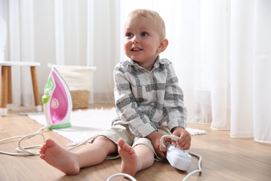 Photo of Little child playing with power strip and iron plug on floor at home. Dangerous situation