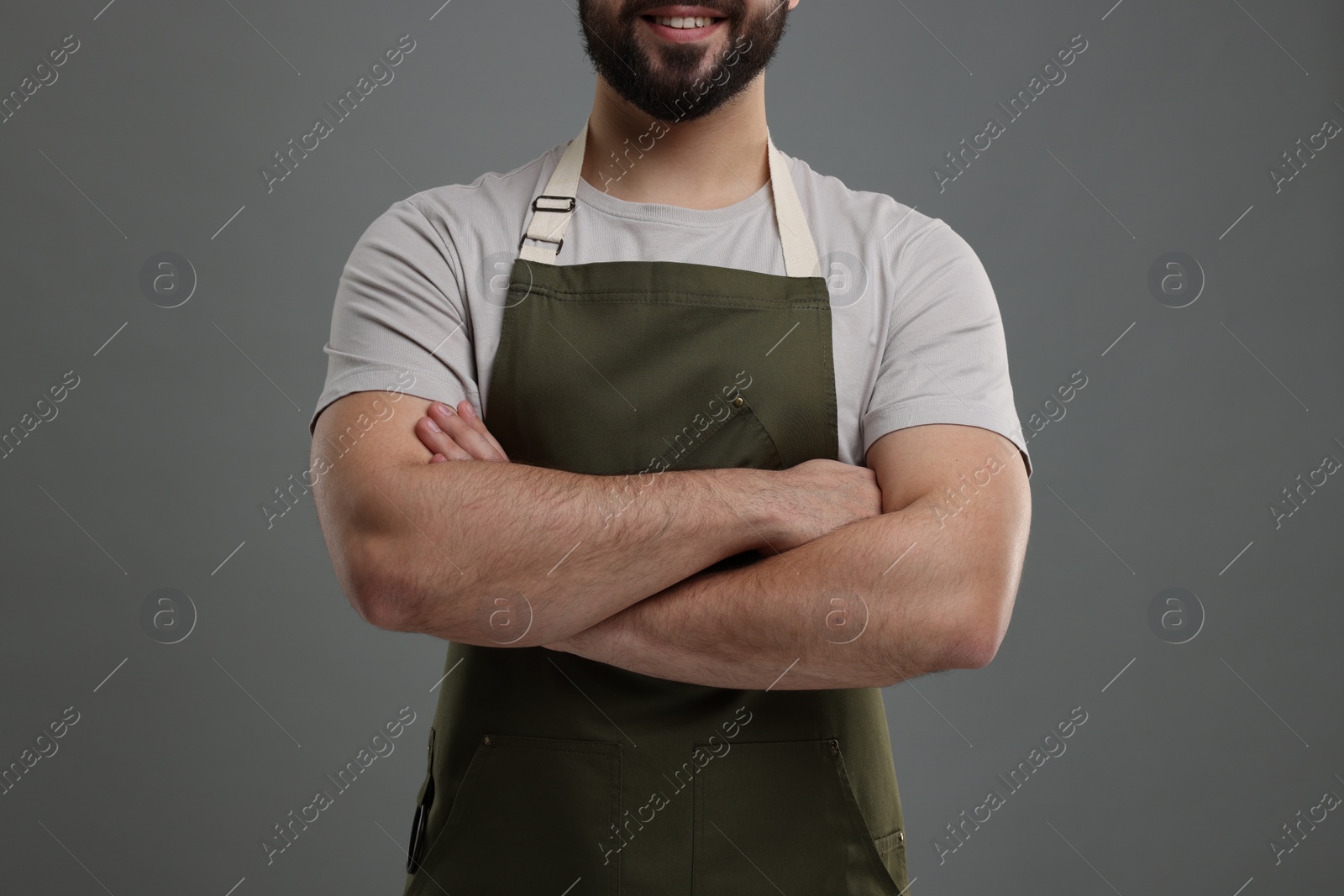 Photo of Smiling man in kitchen apron with crossed arms on grey background, closeup. Mockup for design