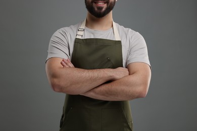 Photo of Smiling man in kitchen apron with crossed arms on grey background, closeup. Mockup for design