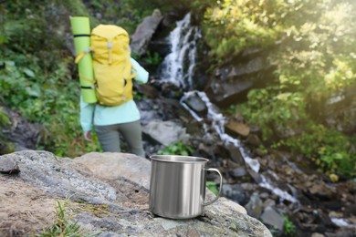 Tourist near waterfall in mountains, focus on cup