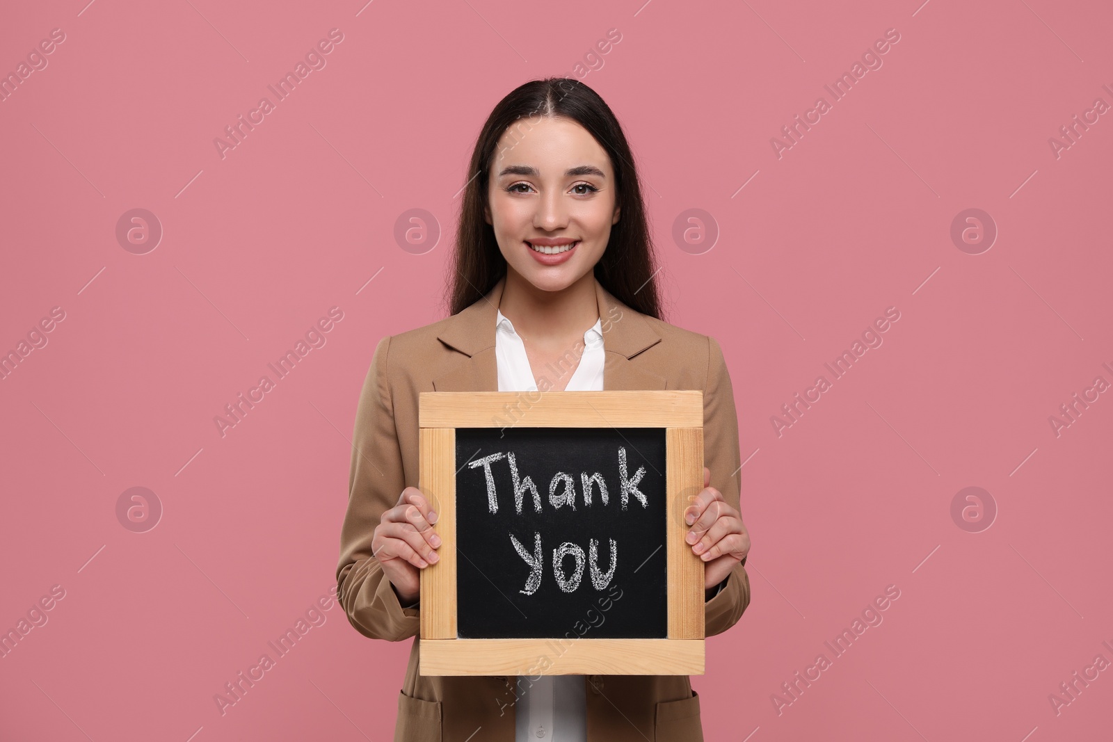 Photo of Happy woman holding small chalkboard with phrase Thank You on pink background