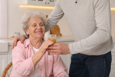 Photo of Young caregiver giving drink to senior woman in kitchen. Home care service