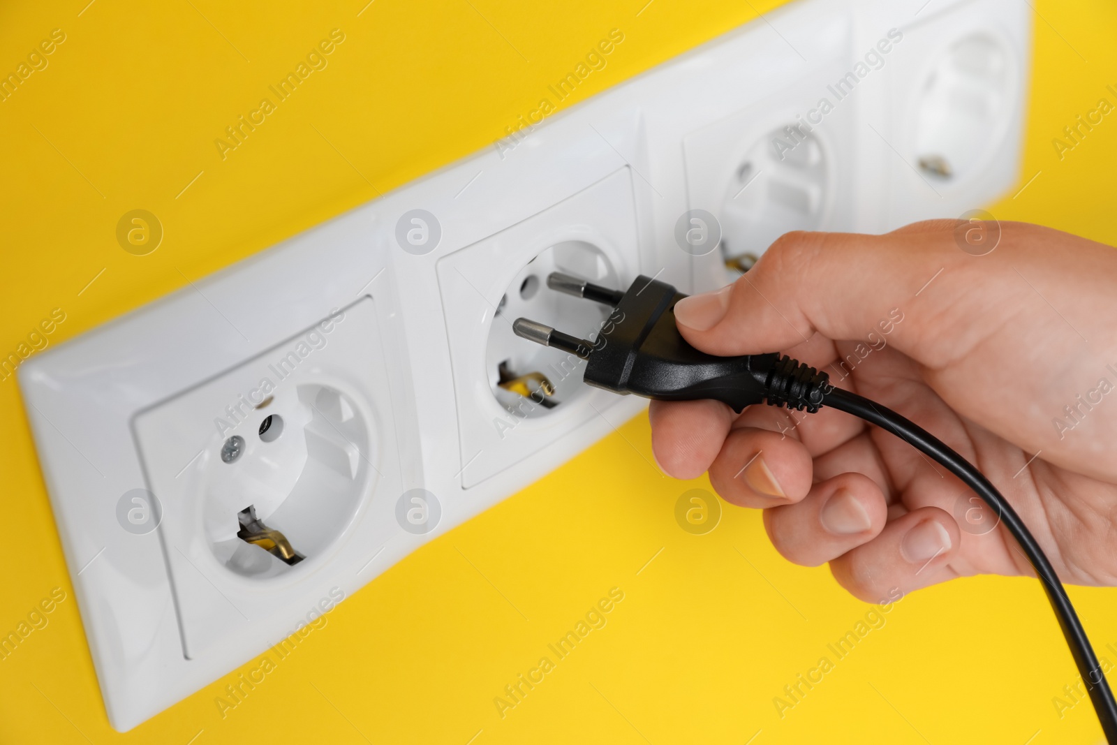Photo of Woman inserting plug into power socket on yellow wall, closeup. Electrical supply