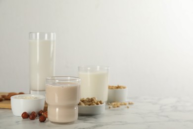 Photo of Different vegan milks and ingredients on white marble table. Space for text