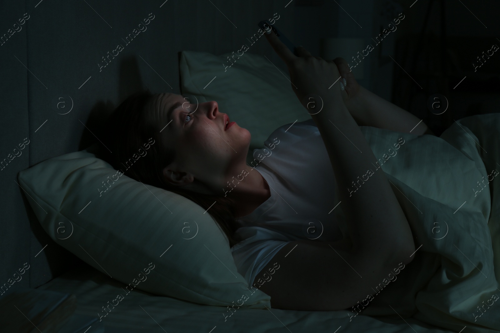 Photo of Woman using smartphone on bed at night. Internet addiction