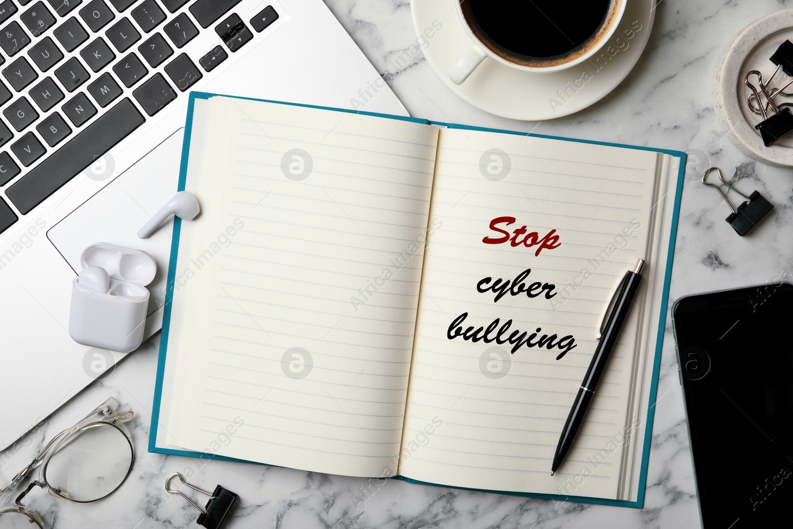 Image of Notebook with phrase STOP CYBER BULLYING and laptop on marble table, flat lay 