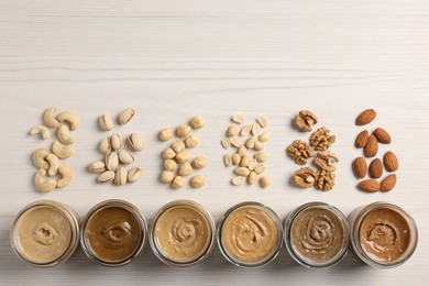 Photo of Many tasty nut butters in jars and nuts on white wooden table, flat lay. Space for text
