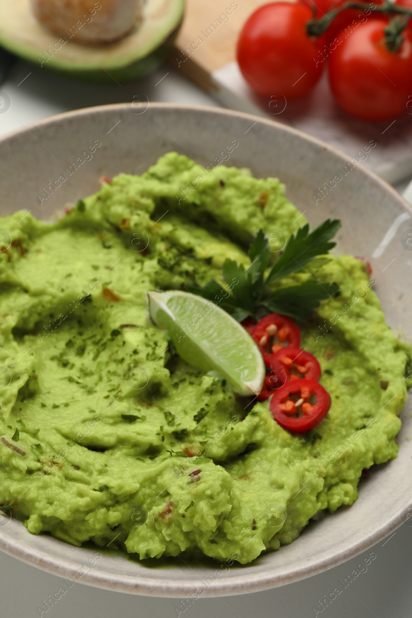 Photo of Bowl of delicious guacamole served with lime, pepper and parsley on table