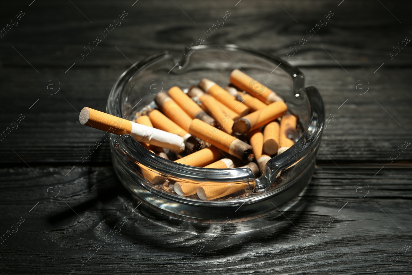 Photo of Glass ashtray with cigarette stubs on black wooden table