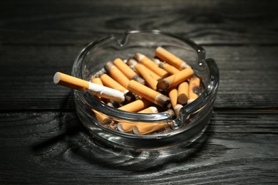 Glass ashtray with cigarette stubs on black wooden table
