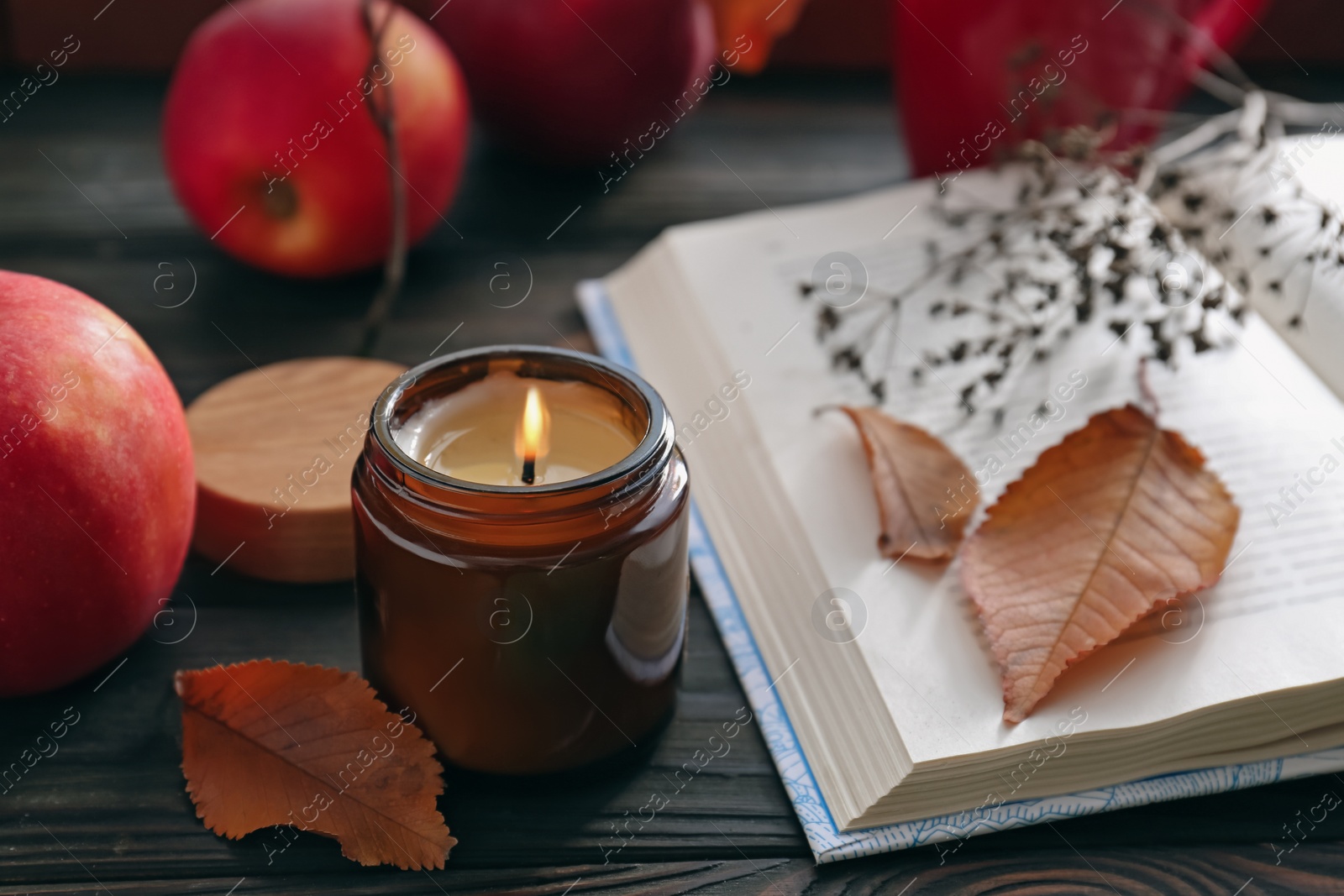 Photo of Beautiful burning candle and book on wooden table. Autumn atmosphere