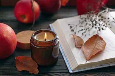 Photo of Beautiful burning candle and book on wooden table. Autumn atmosphere