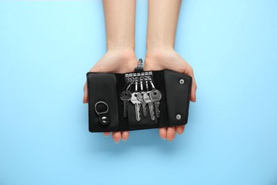 Woman holding open leather holder with keys on light blue background, top view