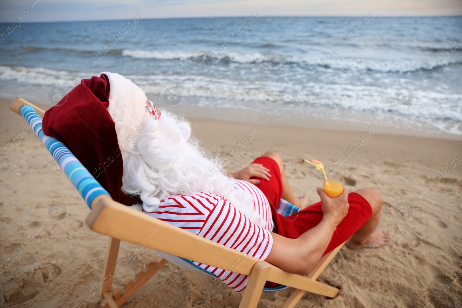 Photo of Santa Claus with cocktail relaxing in chair on beach. Christmas vacation