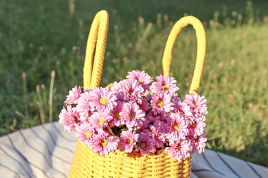 Yellow wicker bag with beautiful flowers on blanket outdoors