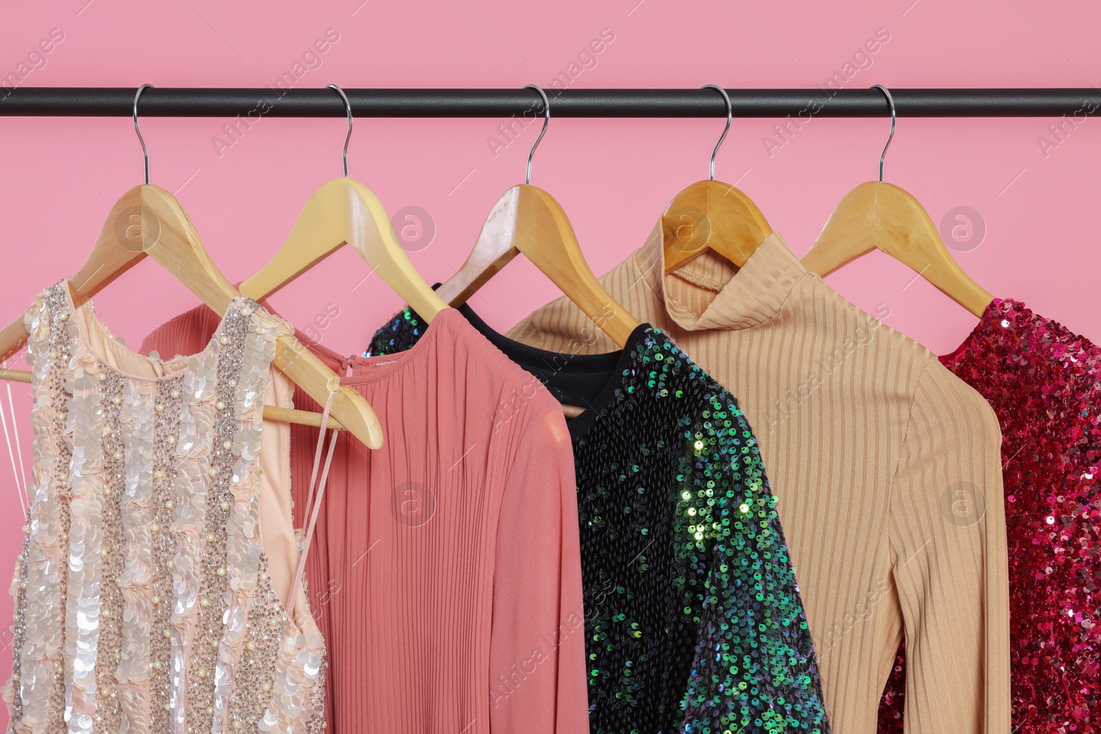 Photo of Rack with stylish women's clothes on wooden hangers against pink background, closeup