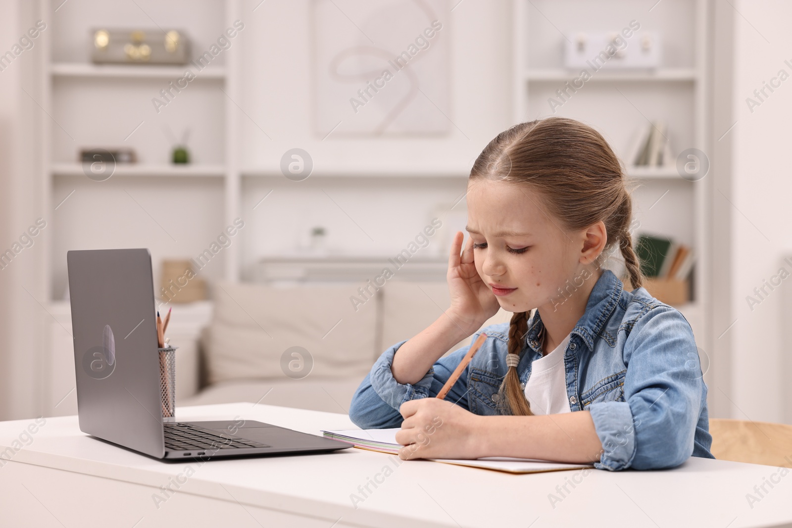 Photo of Little girl suffering from headache while doing homework at home