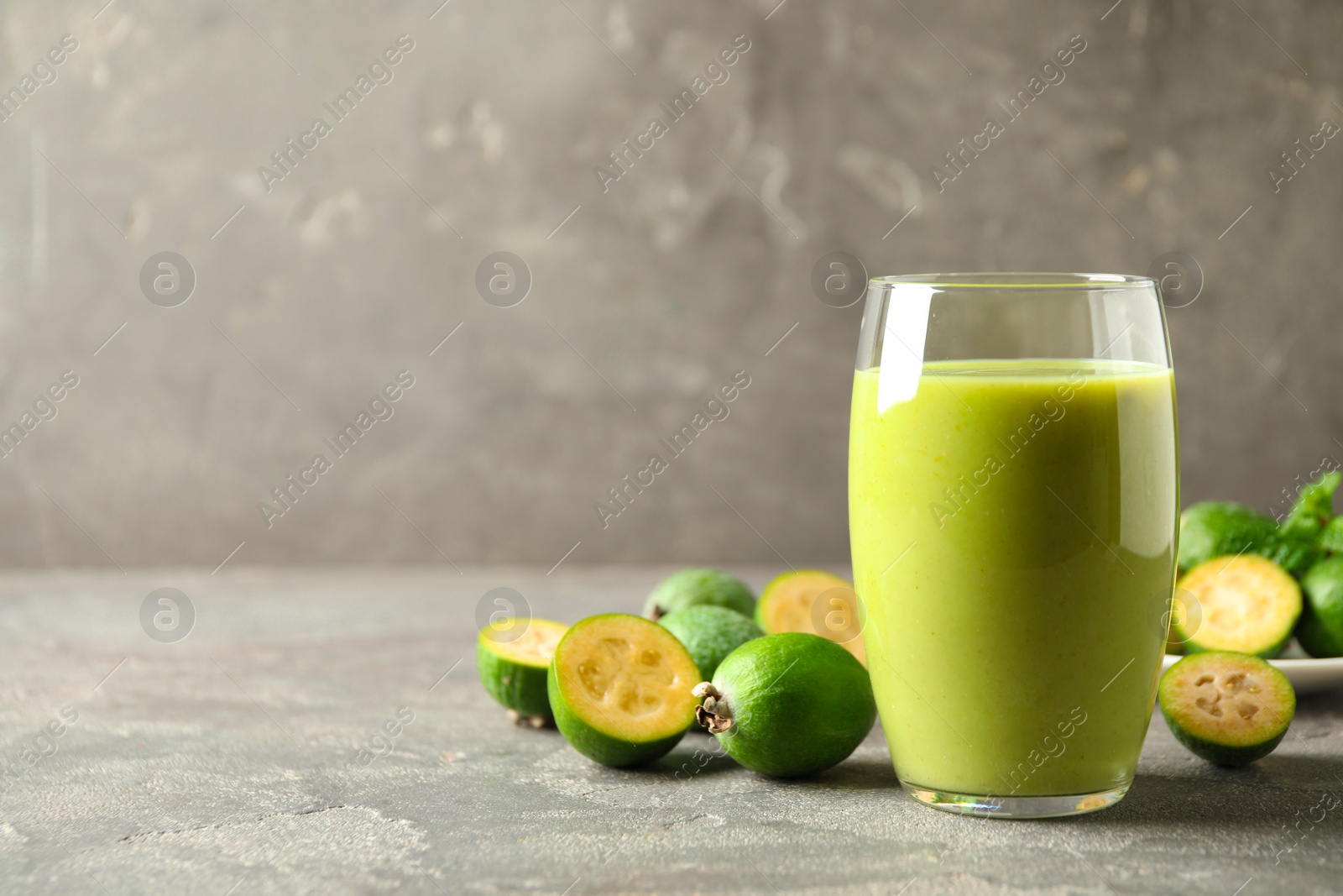 Photo of Fresh feijoa smoothie and fresh fruits on grey table, closeup. Space for text